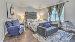 A modern bedroom with a large bed, two sofas, a nightstand, and a window with curtains.