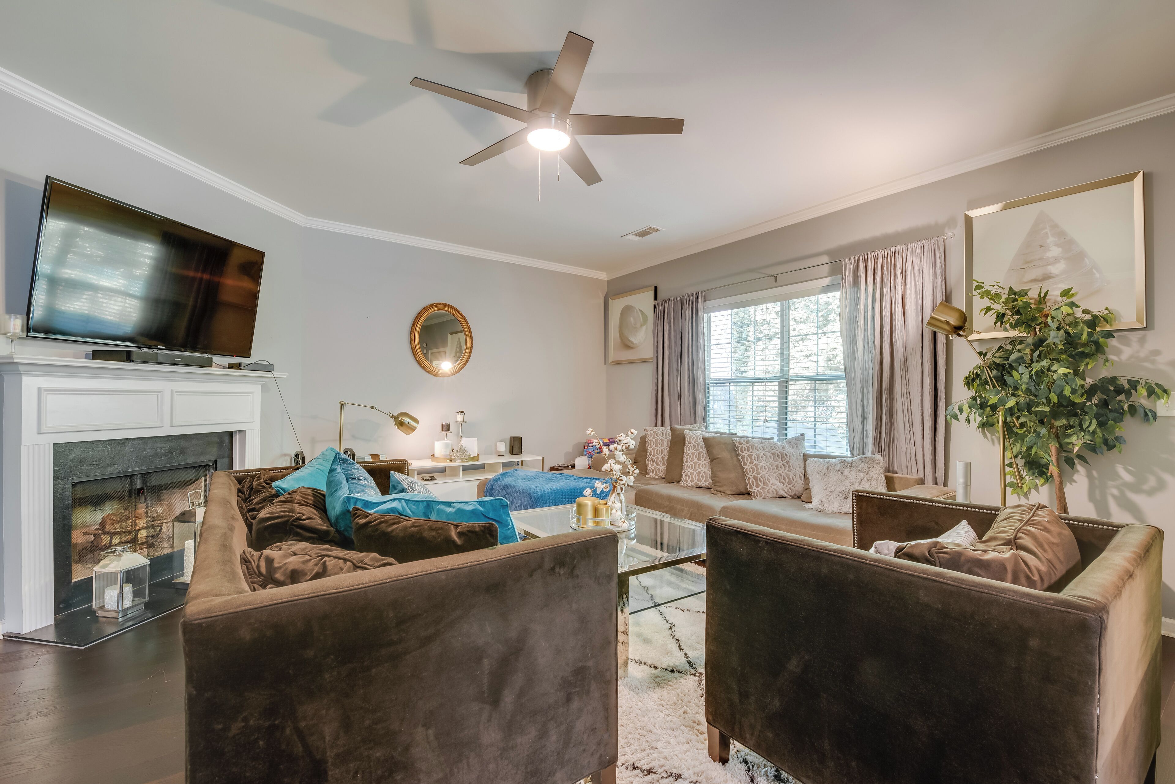 A modern living room with a fireplace, comfortable seating, a ceiling fan, and a large window with curtains.