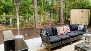 An outdoor patio area with a black wicker sofa, a metal grill, and a metal table with a silver bowl. - Snellville Abode < 9 Mi to Stone Mtn Park! (Snellville)