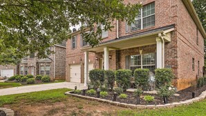 A two-story brick house with a covered porch, a front yard with trimmed bushes, and a visible garage door. - Snellville Abode < 9 Mi to Stone Mtn Park! (Snellville)
