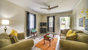 A living room with a sofa, a coffee table, a TV, and a ceiling fan. - Charming Newport News Cottage < 1 Mi to Ocean! (Newport News)