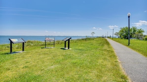 A grassy pathway beside a body of water with informational signs and a lamp post. - Charming Newport News Cottage < 1 Mi to Ocean! (Newport News)