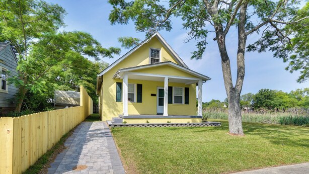 A yellow house with a porch, surrounded by a wooden fence and trees. - Charming Newport News Cottage < 1 Mi to Ocean! (Newport News)