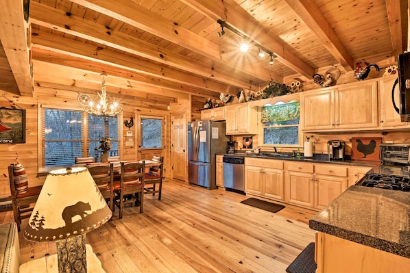 A wooden cabin interior with a dining area, kitchen, and a chandelier.