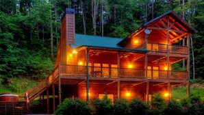 Une cabane en rondins à deux étages, dotée d’un balcon et entourée d’une forêt dense.