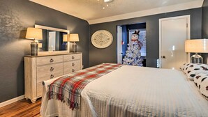 A bedroom with a bed, a dresser, a ceiling fan, a wall-mounted mirror, and a door leading to another room. - Junction City Home: Large Yard & Deck! (Junction City)