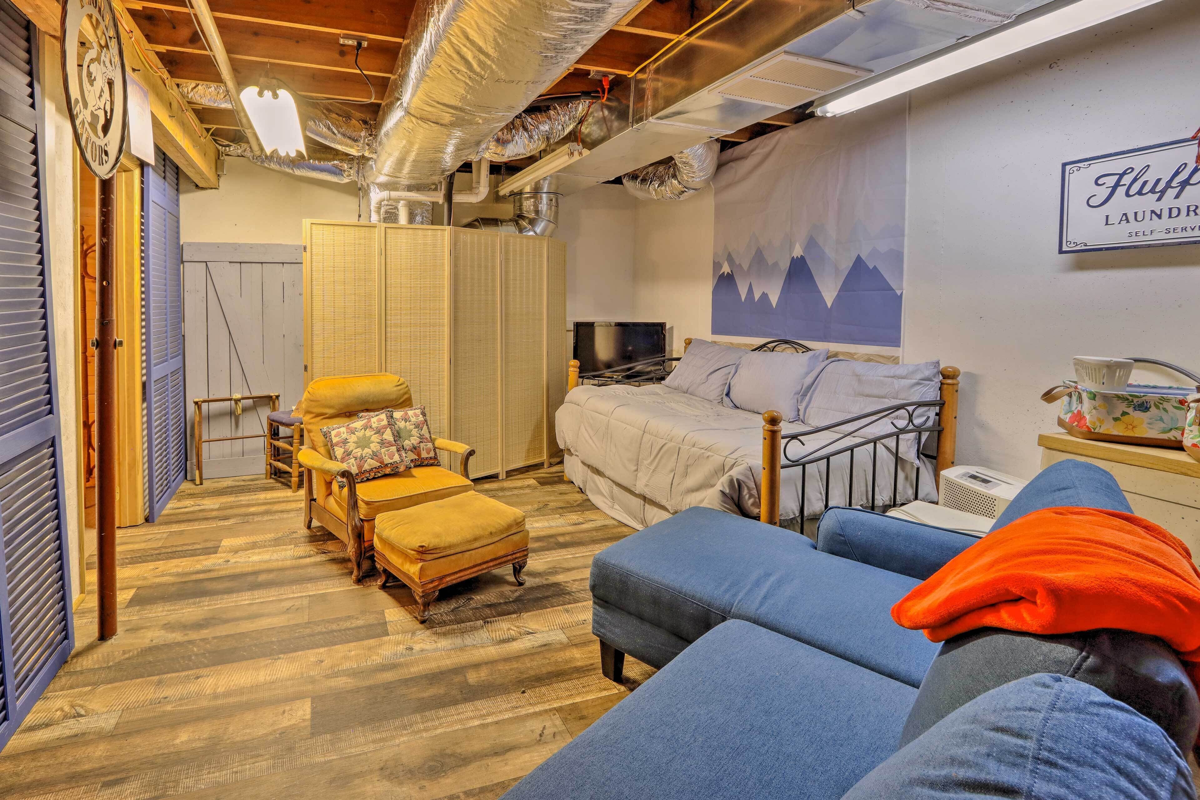 A bedroom with a bed, a sofa, a wooden chest, a television, and a wall-mounted sign.