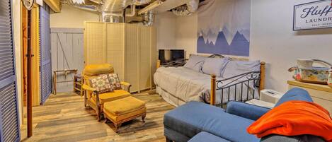 A bedroom with a bed, a sofa, a wooden chest, a television, and a wall-mounted sign.