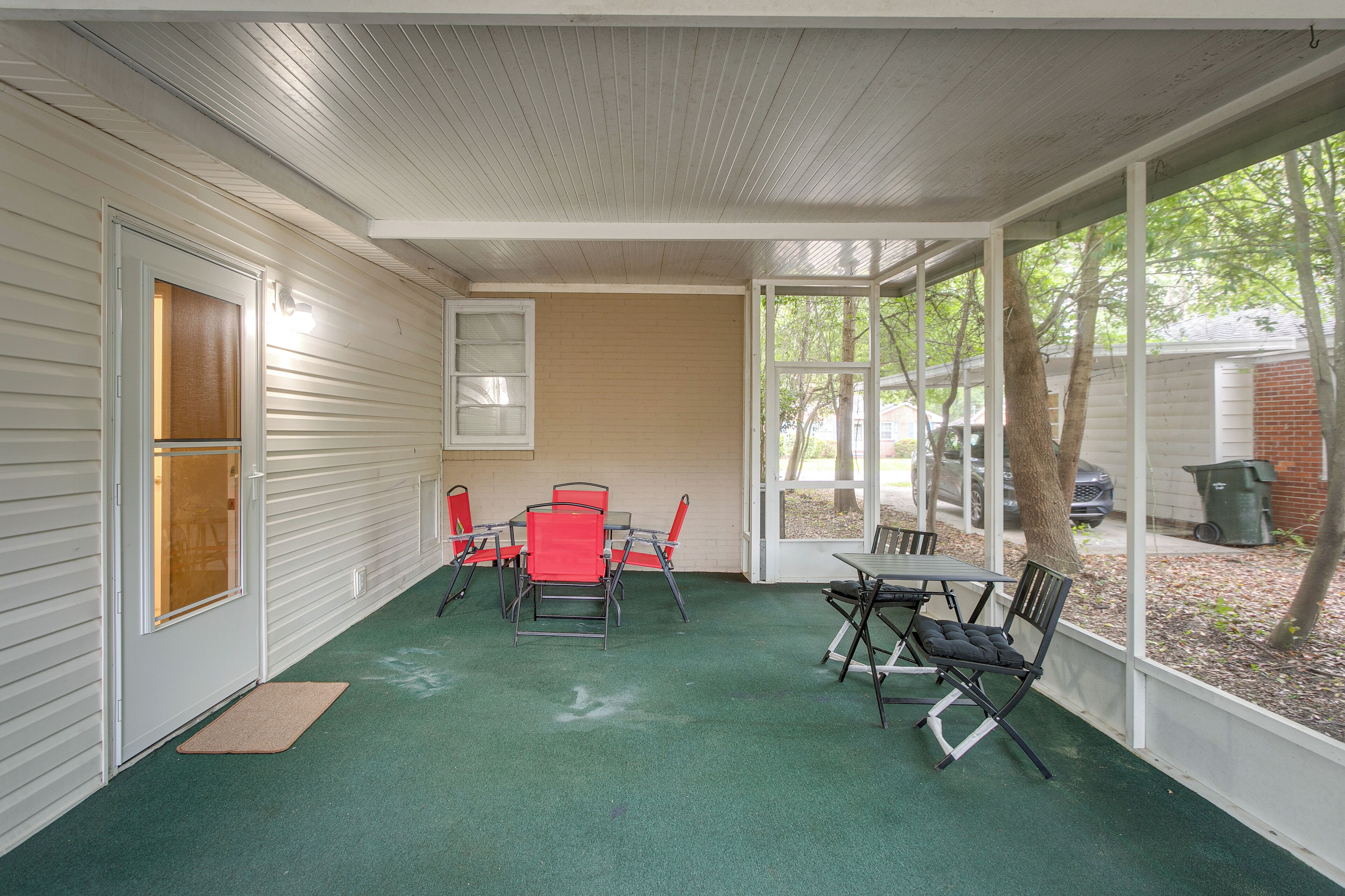 A covered patio with a green floor, white walls, and a window overlooking a backyard.