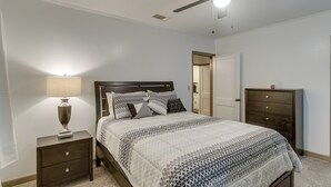 Een slaapkamer met een bed, nachtkastje, dressoir en plafondventilator.