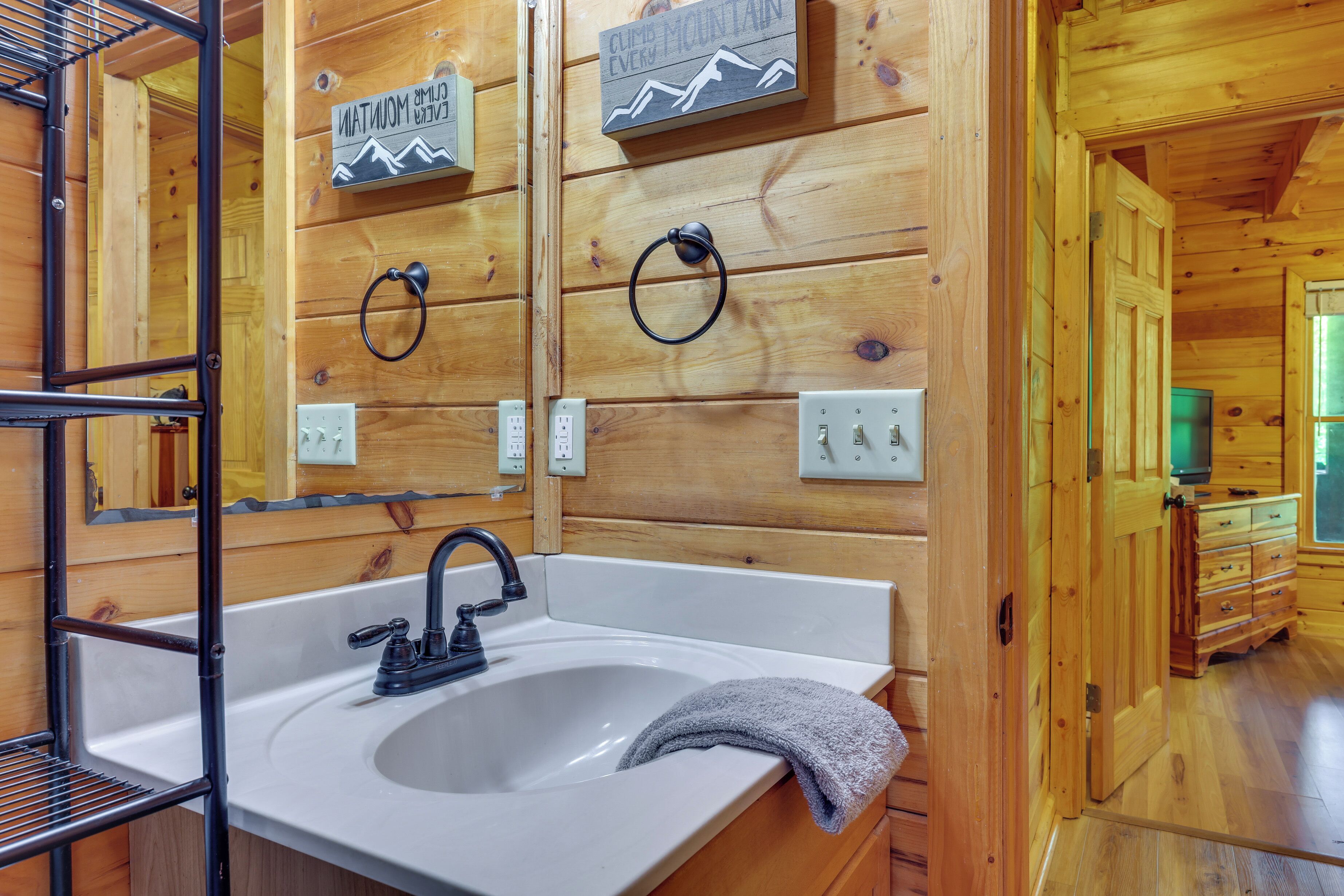 Interior de una cabaña de madera con un lavamanos blanco, grifo negro y una toalla sobre la encimera.