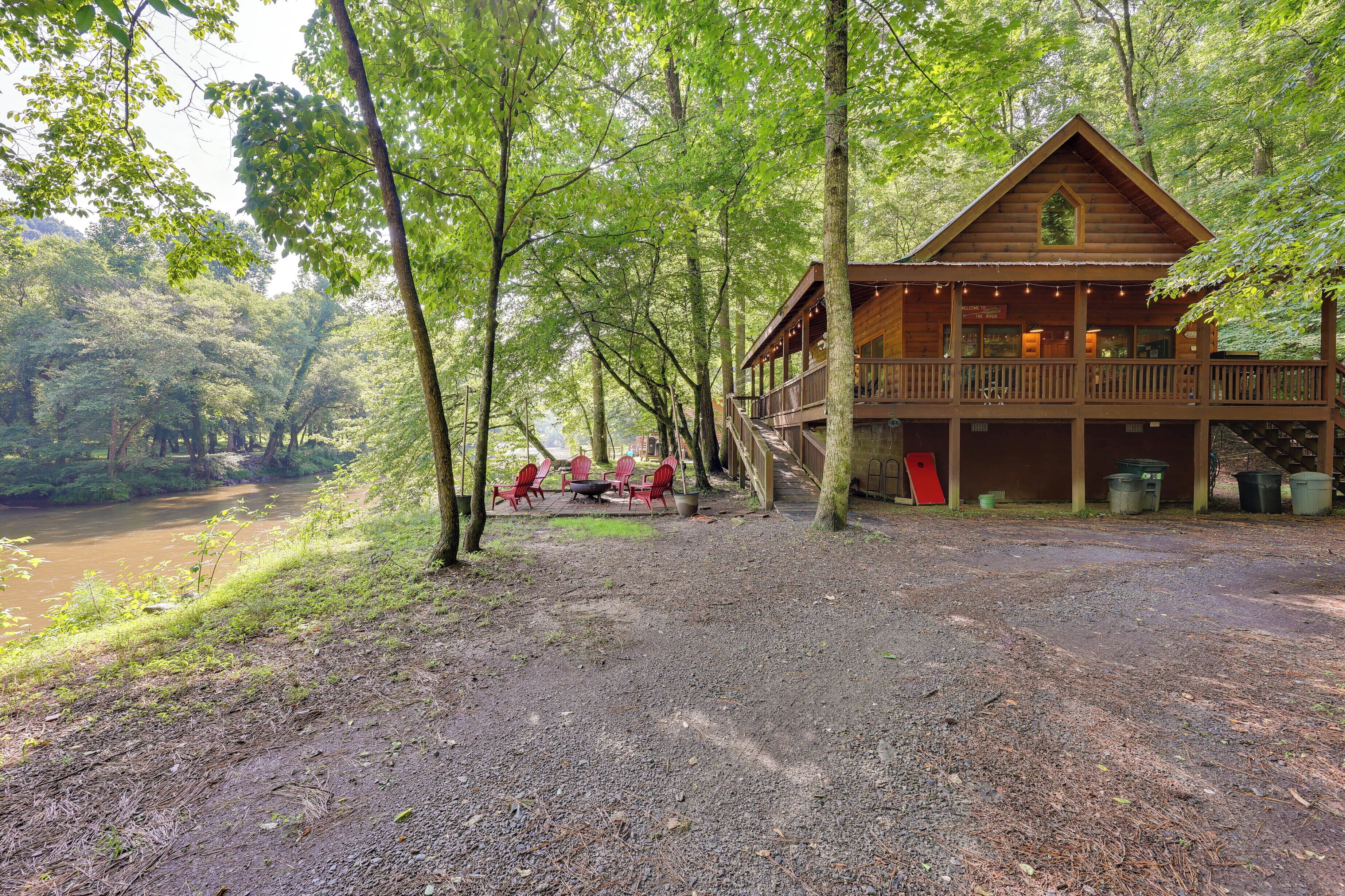 Une cabane dotée d’un porche et d’un espace extérieur aménagé pour s’asseoir, entourée d’arbres et bordée par une rivière.