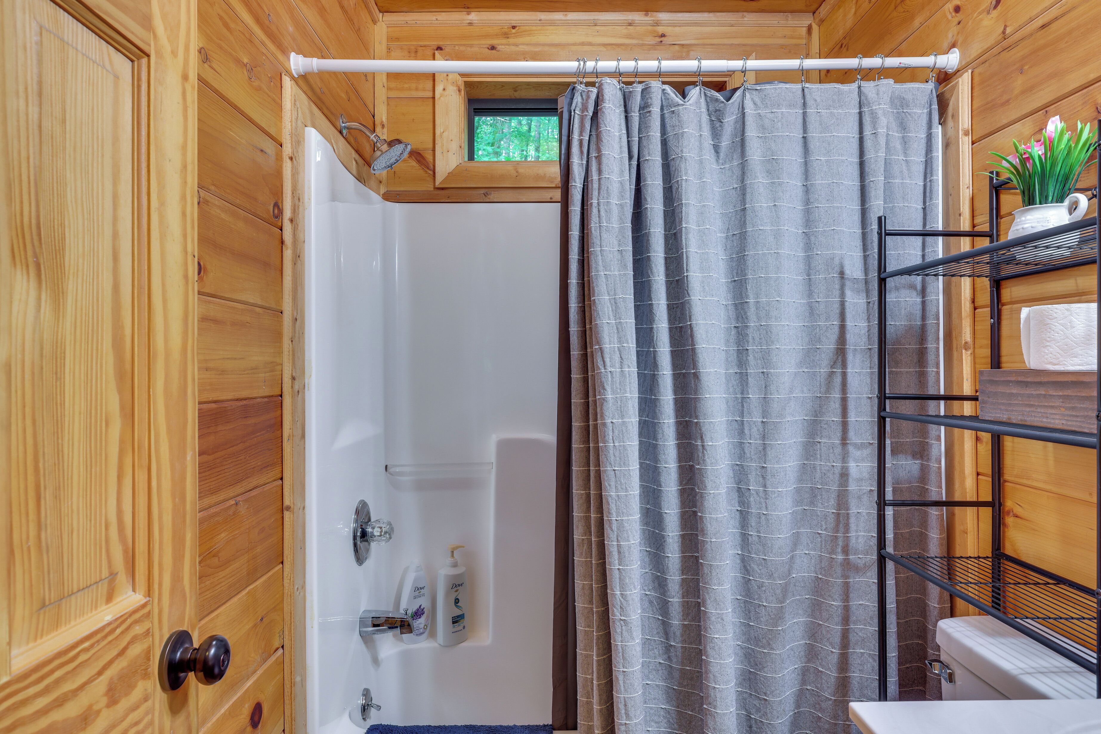Un baño de madera con ducha, un perchero y una repisa con artículos de tocador.