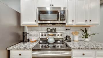 A kitchen with white cabinets, a stainless steel microwave, a coffee maker, and a kettle.