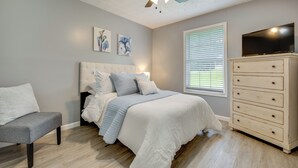 A bedroom with a bed, a dresser, a chair, a ceiling fan, and artwork on the wall.