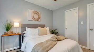 A bedroom with a bed, bedside table, lamp, and a wall-mounted artwork.