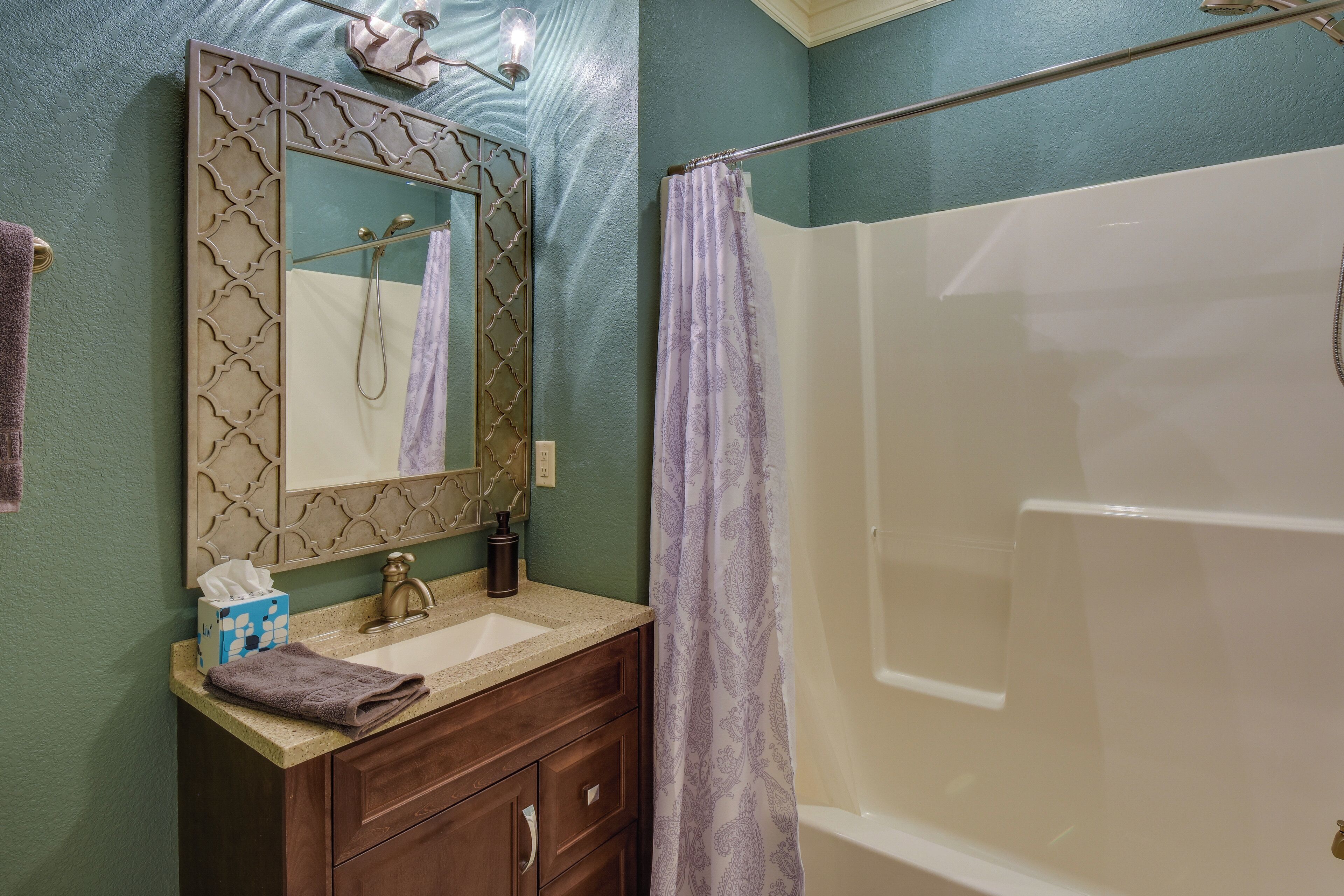 A bathroom with a vanity, sink, mirror, and shower.