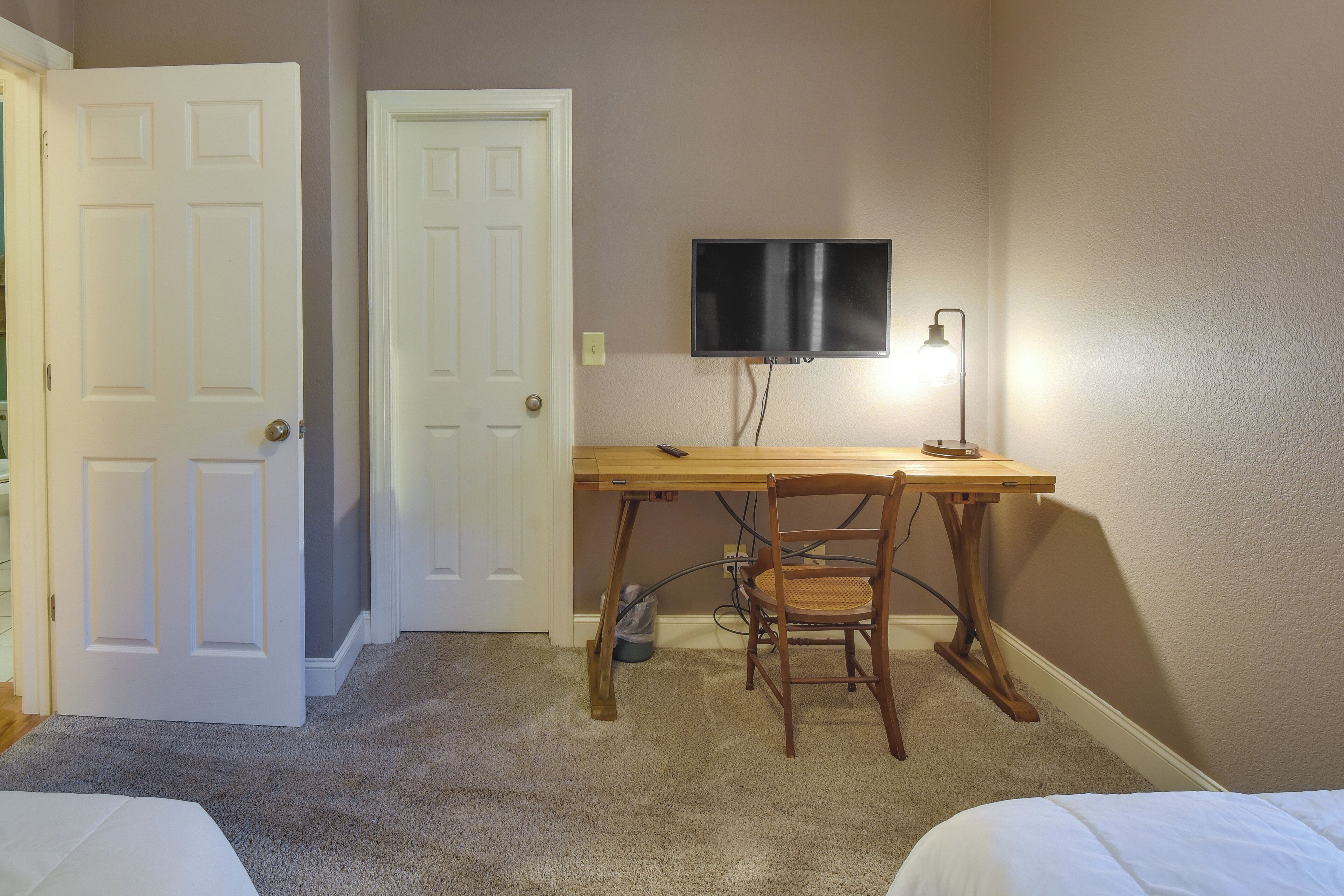 A room with a wooden desk, a chair, a television mounted on the wall, and two white doors.