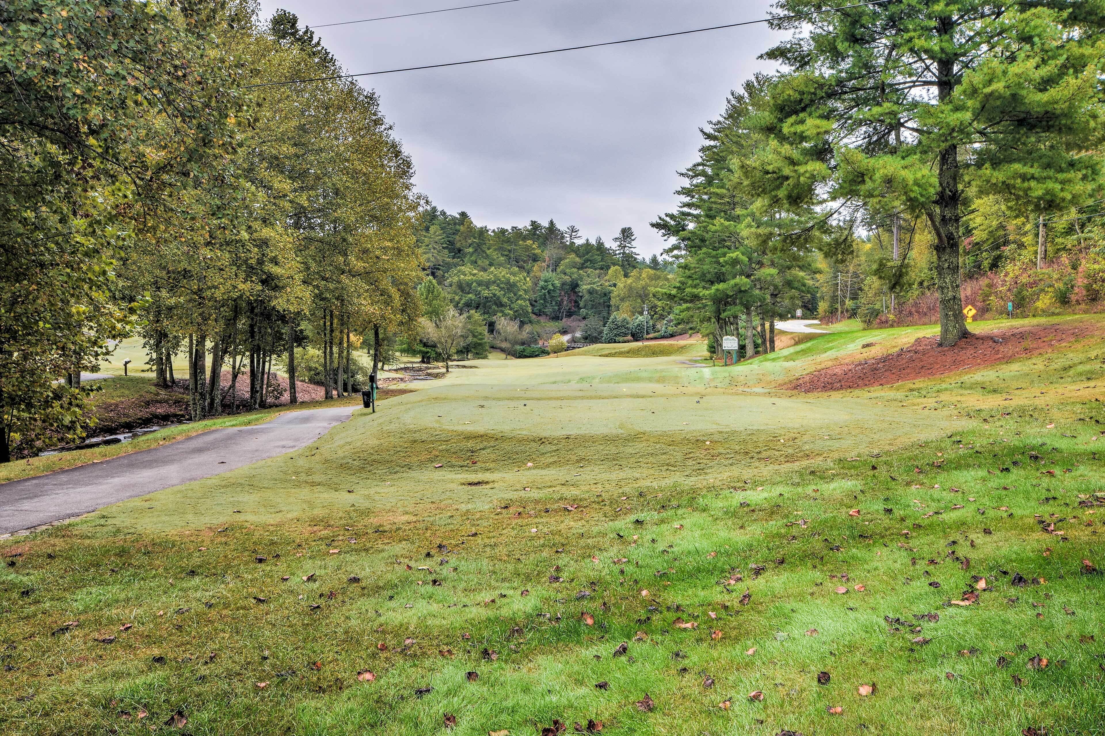 A golf course with a well-maintained fairway, surrounded by trees and a clear sky.