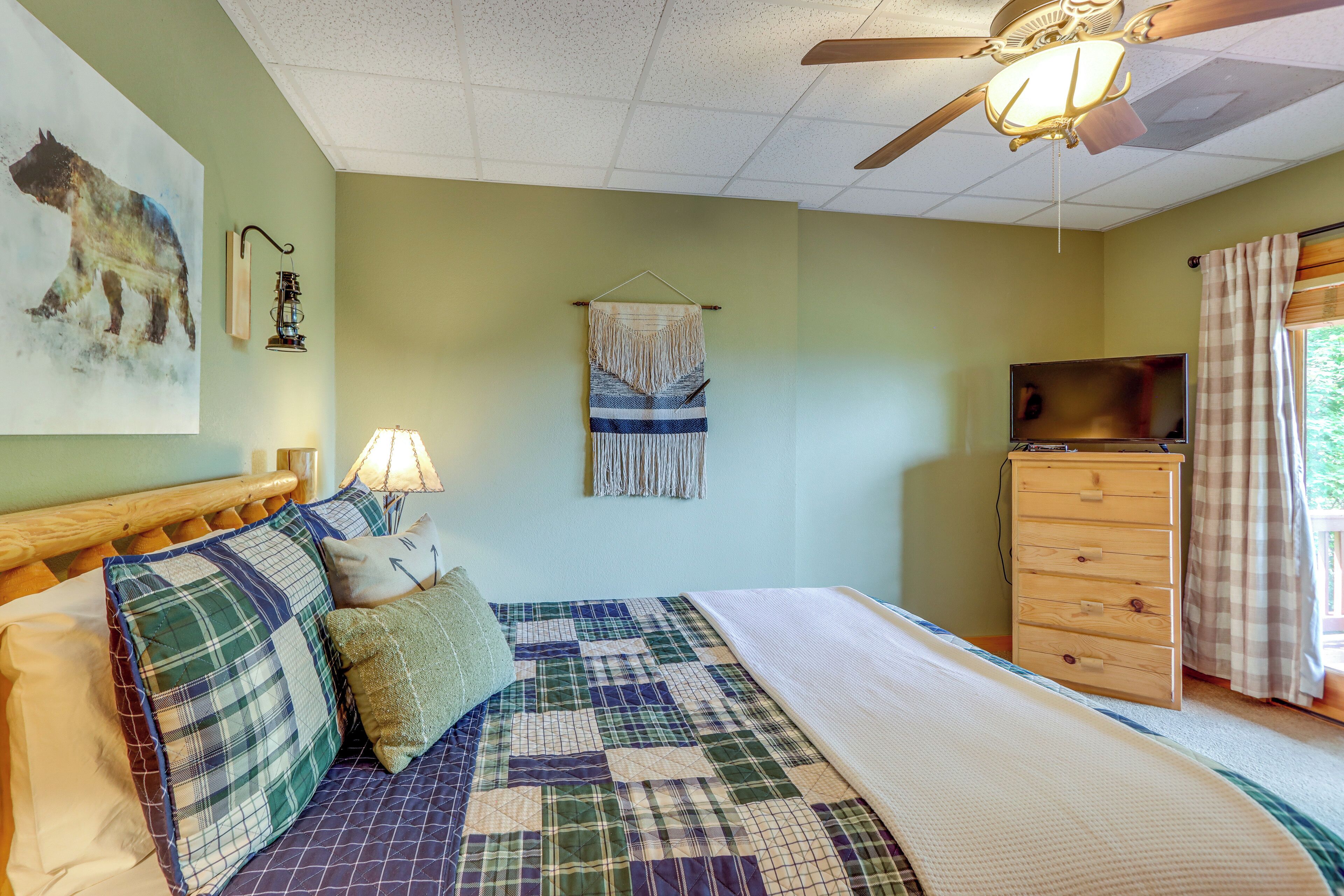 Un dormitorio con una cama, un aparador de madera, un televisor, un objeto decorativo en la pared y un ventilador de techo.