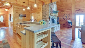 Ein Holzhütten-Interieur mit Kücheninsel, Kamin aus Stein und Holzbalkendecke.