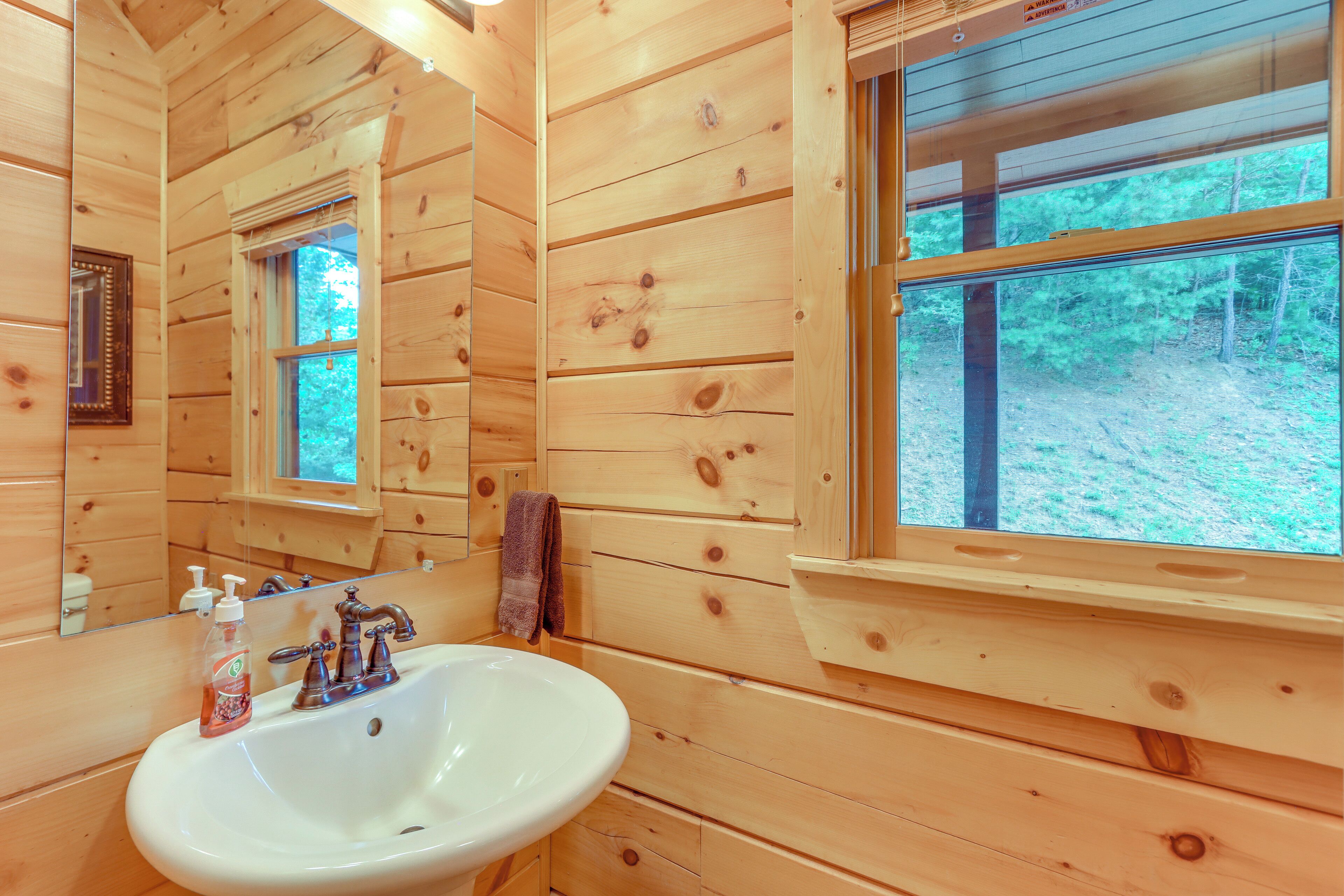 A wooden cabin bathroom with a sink, mirror, and windows.