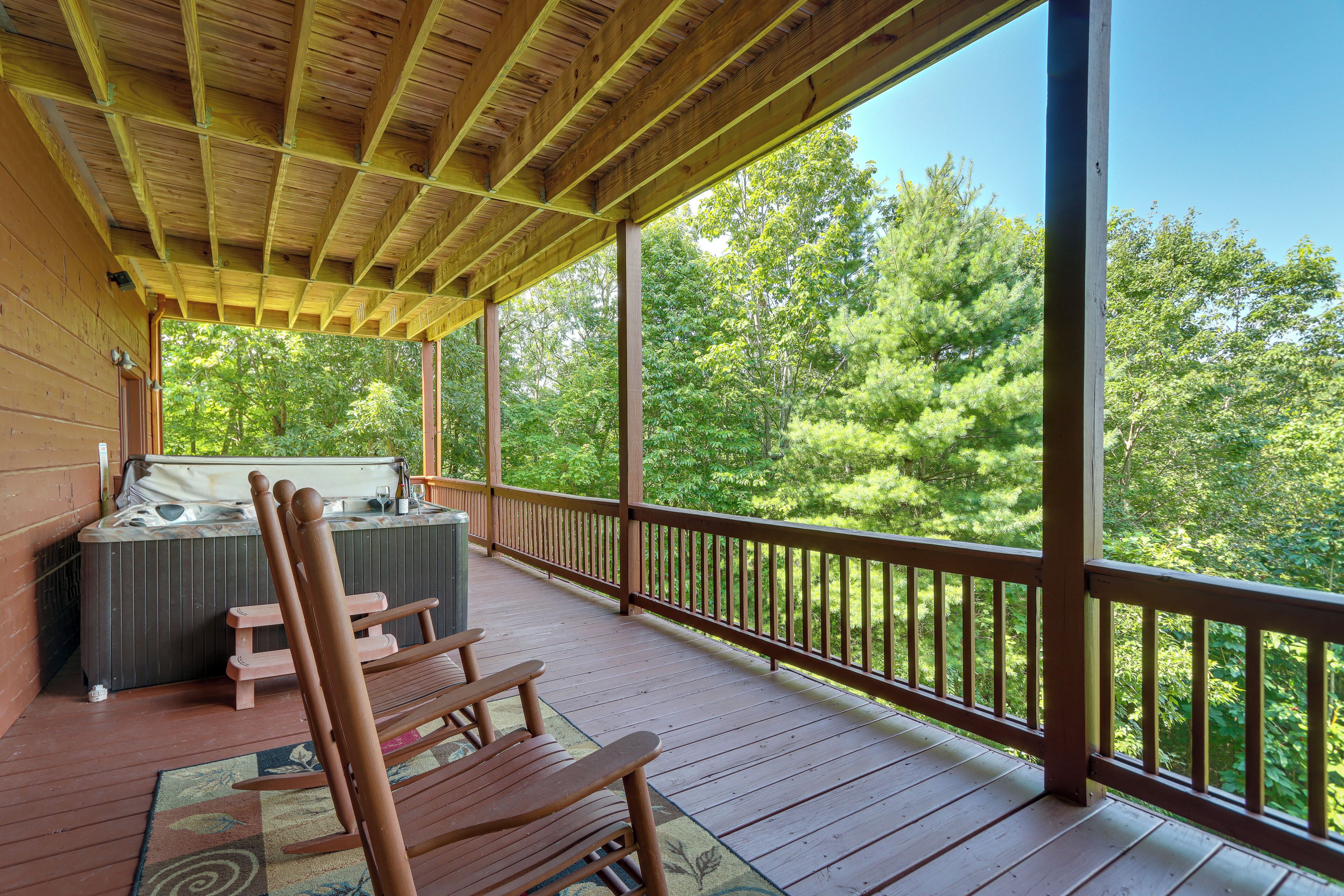 A wooden deck with a hot tub and seating area, overlooking a forested area.