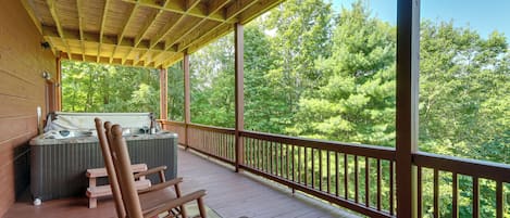 A wooden deck with a hot tub and seating area, overlooking a forested area.