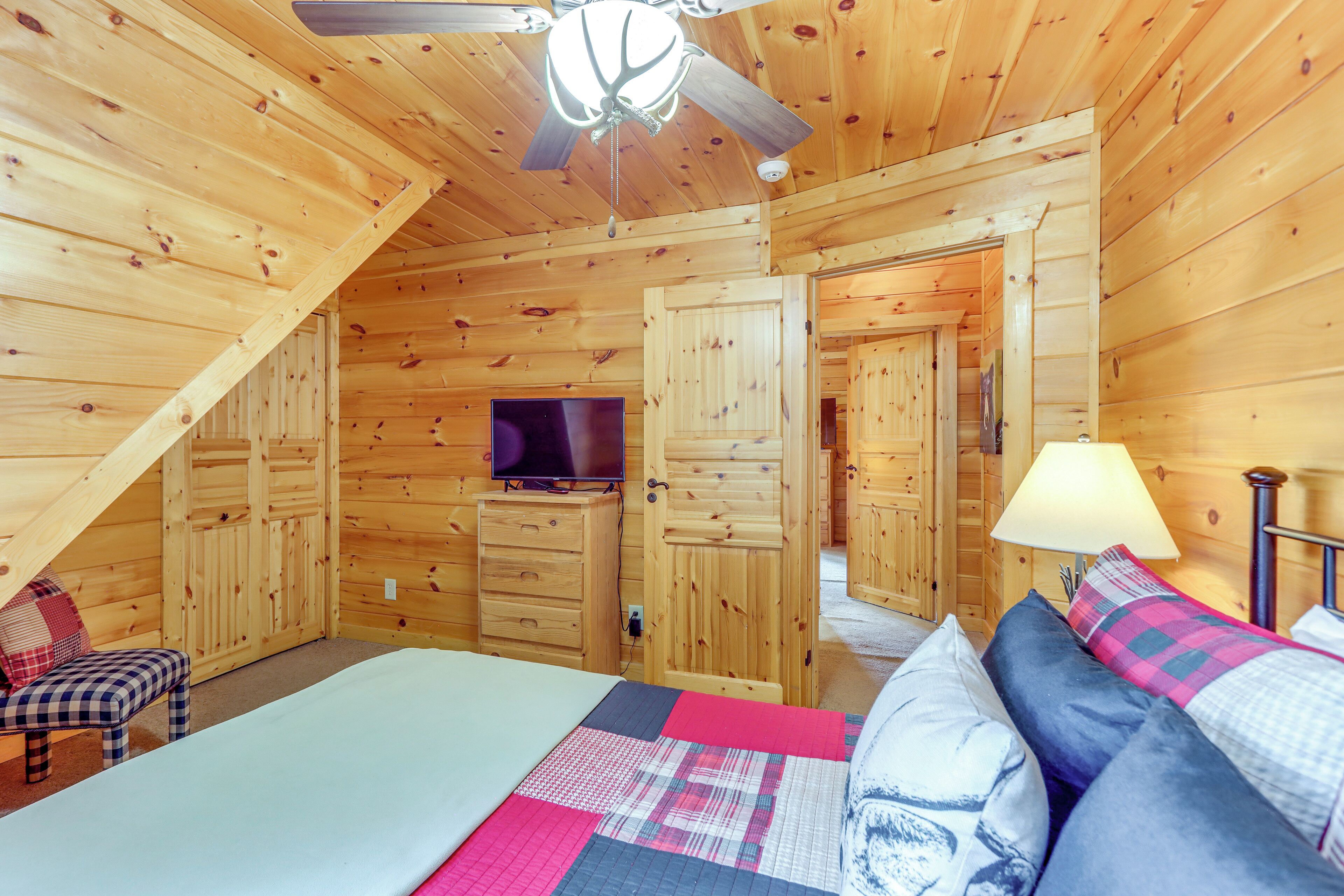 Una habitación cálida tipo cabaña con cama, televisor, escritorio y ventilador de techo.