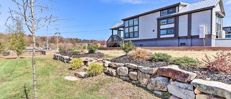 Une maison moderne dotée d’un mur de soutènement en pierre, d’une petite terrasse et d’une pelouse bien entretenue.