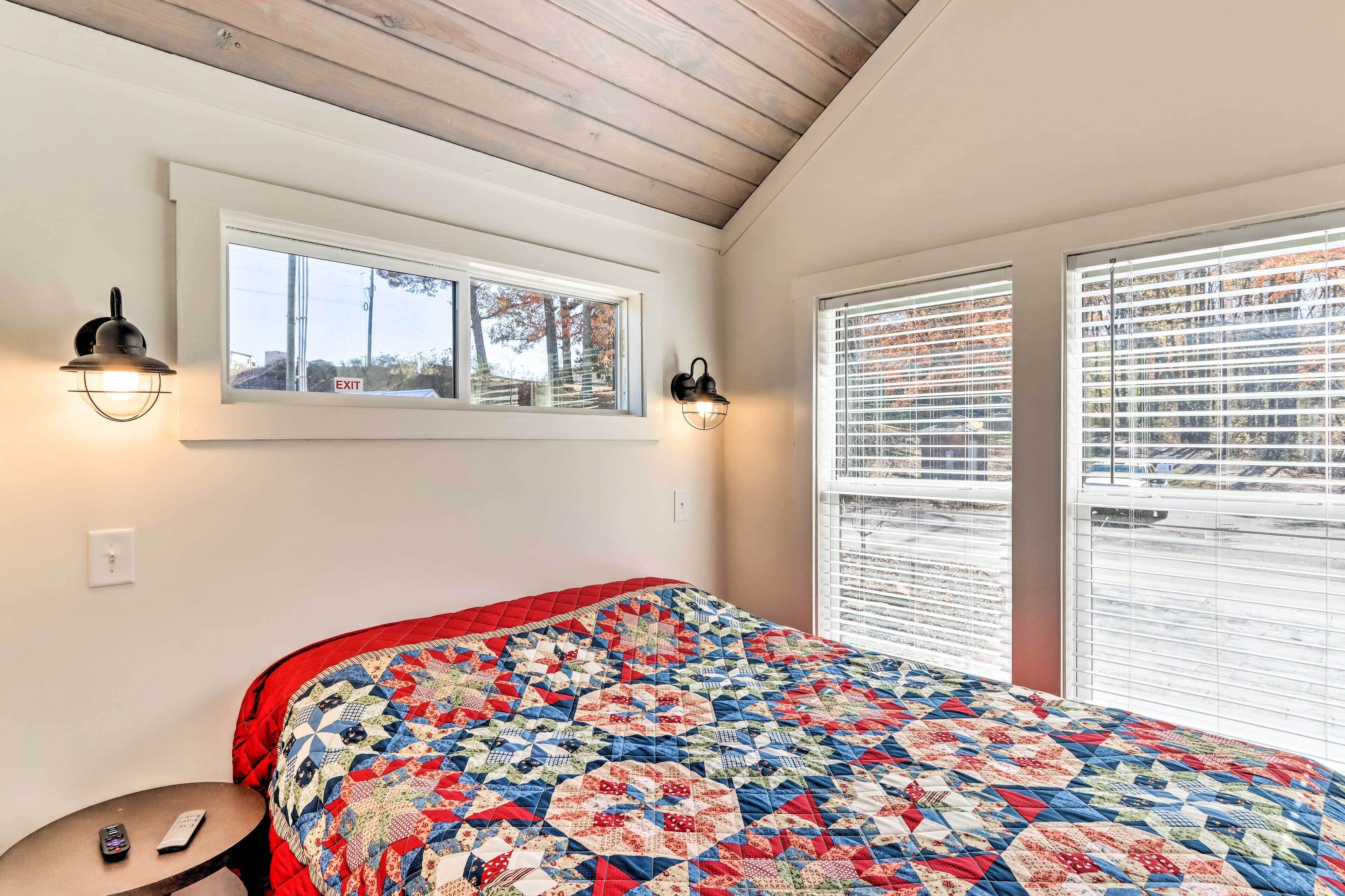 Ein Schlafzimmer mit einem großen Bett, zwei Wandlampen, einem Fenster mit Jalousien und einem kleinen Nachttisch mit Fernbedienung.