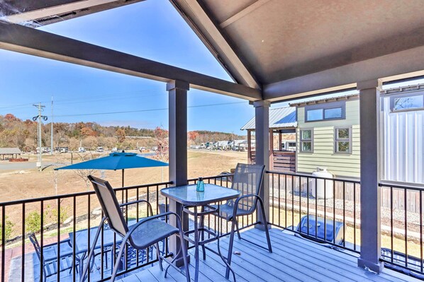 A covered outdoor area with a table and chairs, a blue umbrella, and a view of a building in the background. - Tiny Home Retreat w/ Fire Pit ~ 3 Mi to Lake! (Morganton)