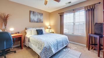 A bedroom with a bed, desk, chair, and a ceiling fan.