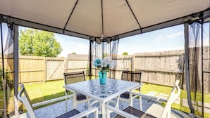 A covered patio with a table and chairs, a vase with flowers, and a wooden fence in the background. - Horn Lake Vacation Rental ~ 14 Mi to Memphis! (Horn Lake)