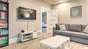 Una sala de estar moderna con un sofá gris, una mesa de centro blanca, un televisor de pantalla plana y una estantería con juegos de mesa.