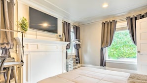 Un dormitorio con cama, televisor montado arriba, escritorio con silla y ventana con cortinas.