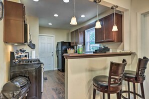 Una cocina con armarios de madera, una estufa y un refrigerador. Hay dos taburetes de bar y una ventana con vistas a zonas verdes.