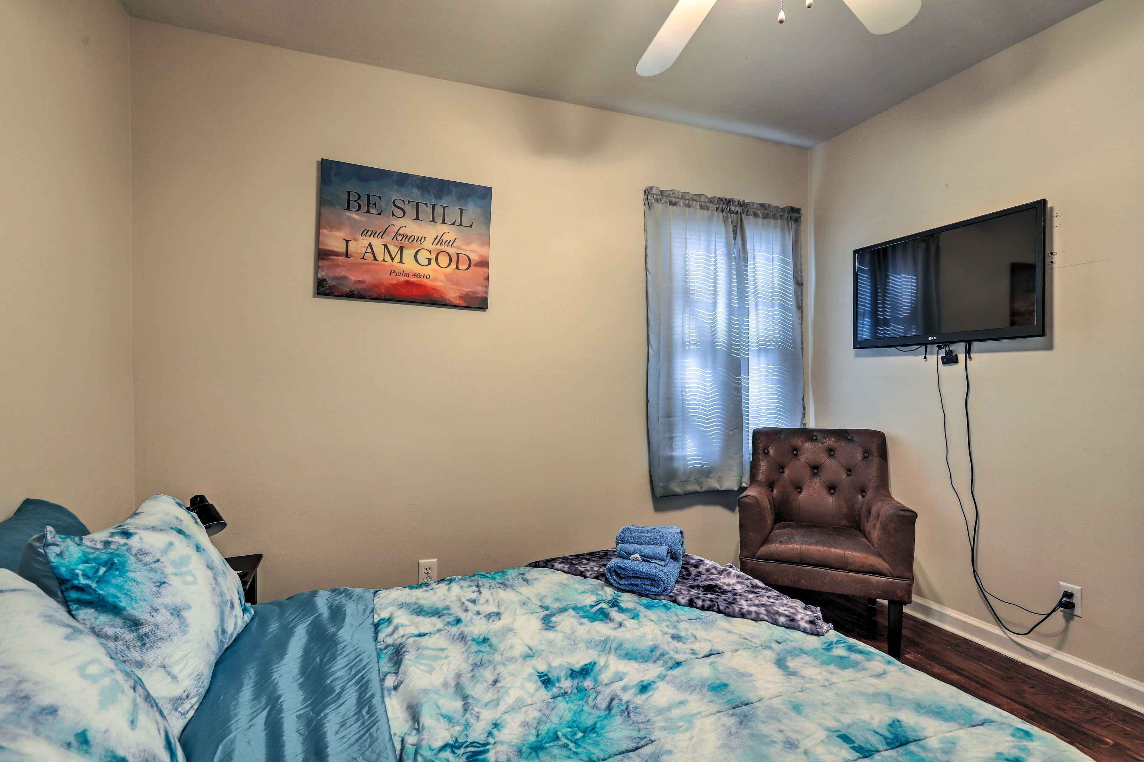 Een slaapkamer met een bed, een stoel, een televisie, een raam met gordijnen en een motiverende quote op de muur.