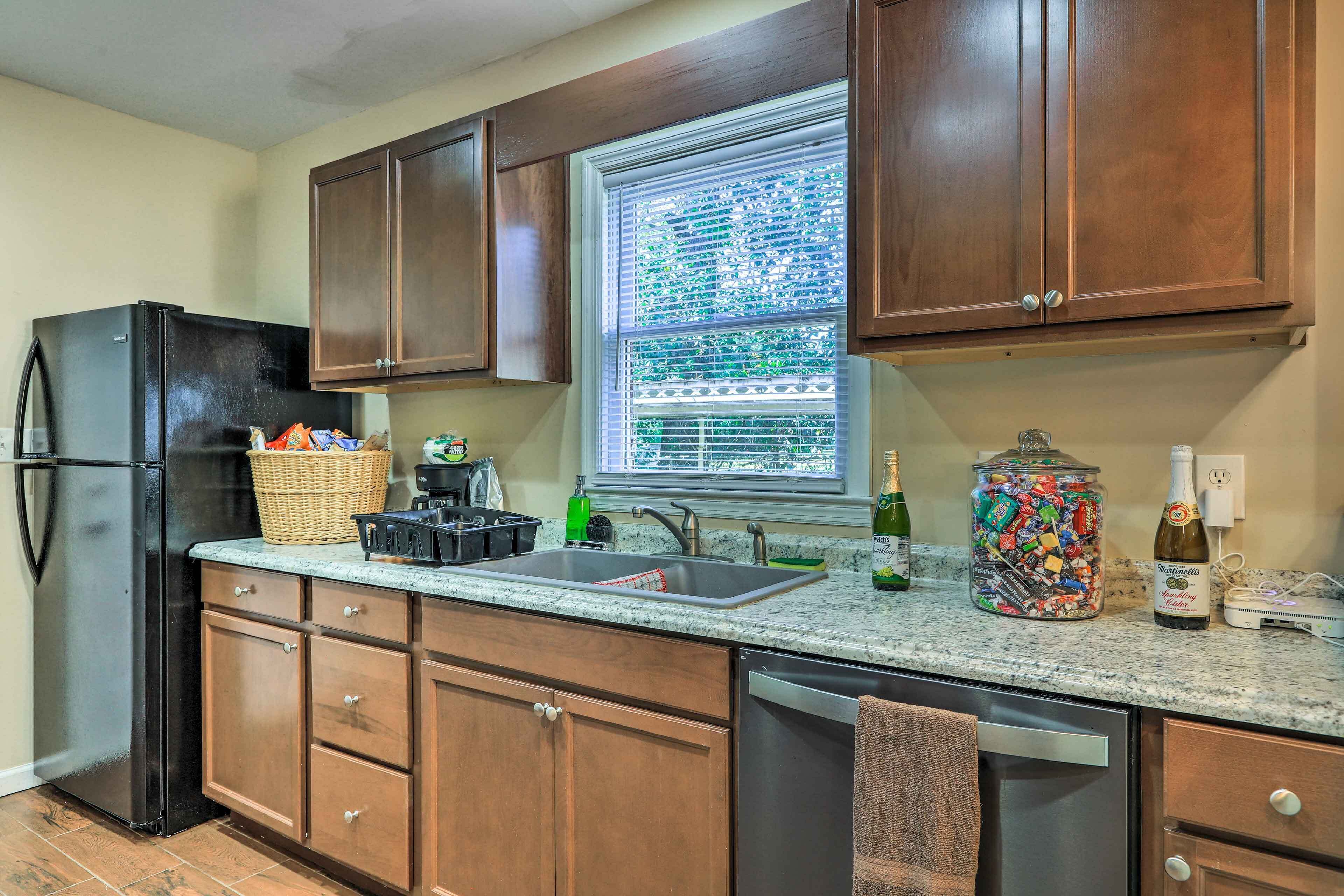 A kitchen with wooden cabinets, a black refrigerator, a window with blinds, a sink, and various kitchen items on the counter.