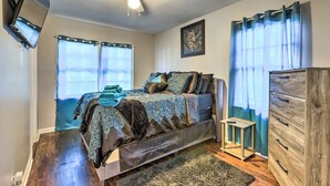 Ein Schlafzimmer mit einem Bett, einem Deckenventilator, einer Kommode und einem Fenster mit Vorhängen.