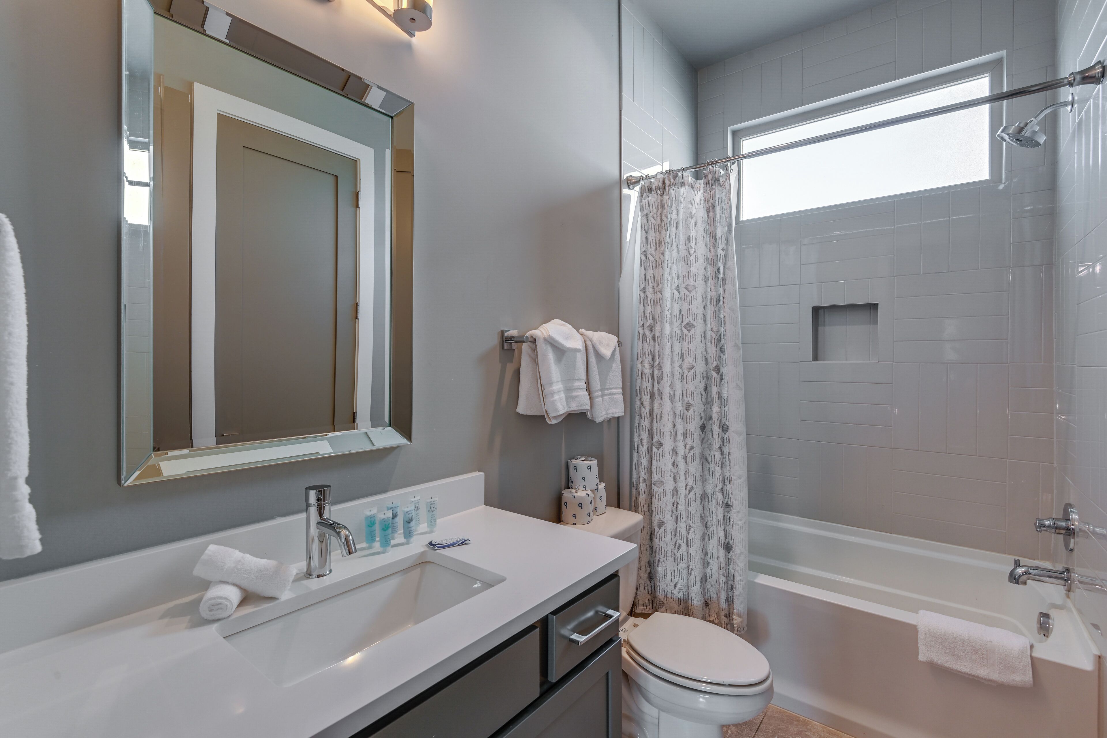 A modern bathroom with a sink, mirror, toilet, and bathtub.
