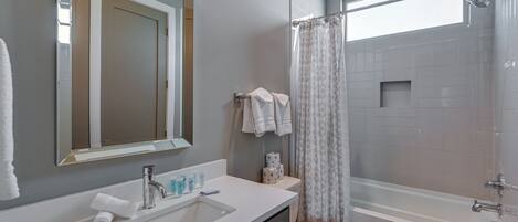 A modern bathroom with a sink, mirror, toilet, and bathtub.