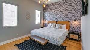 A bedroom with a large bed, a bench, two bedside tables, a TV mounted on the wall, and patterned wallpaper. - Nashville Townhome w/ Rooftop Balcony & Game Room! (Nashville)