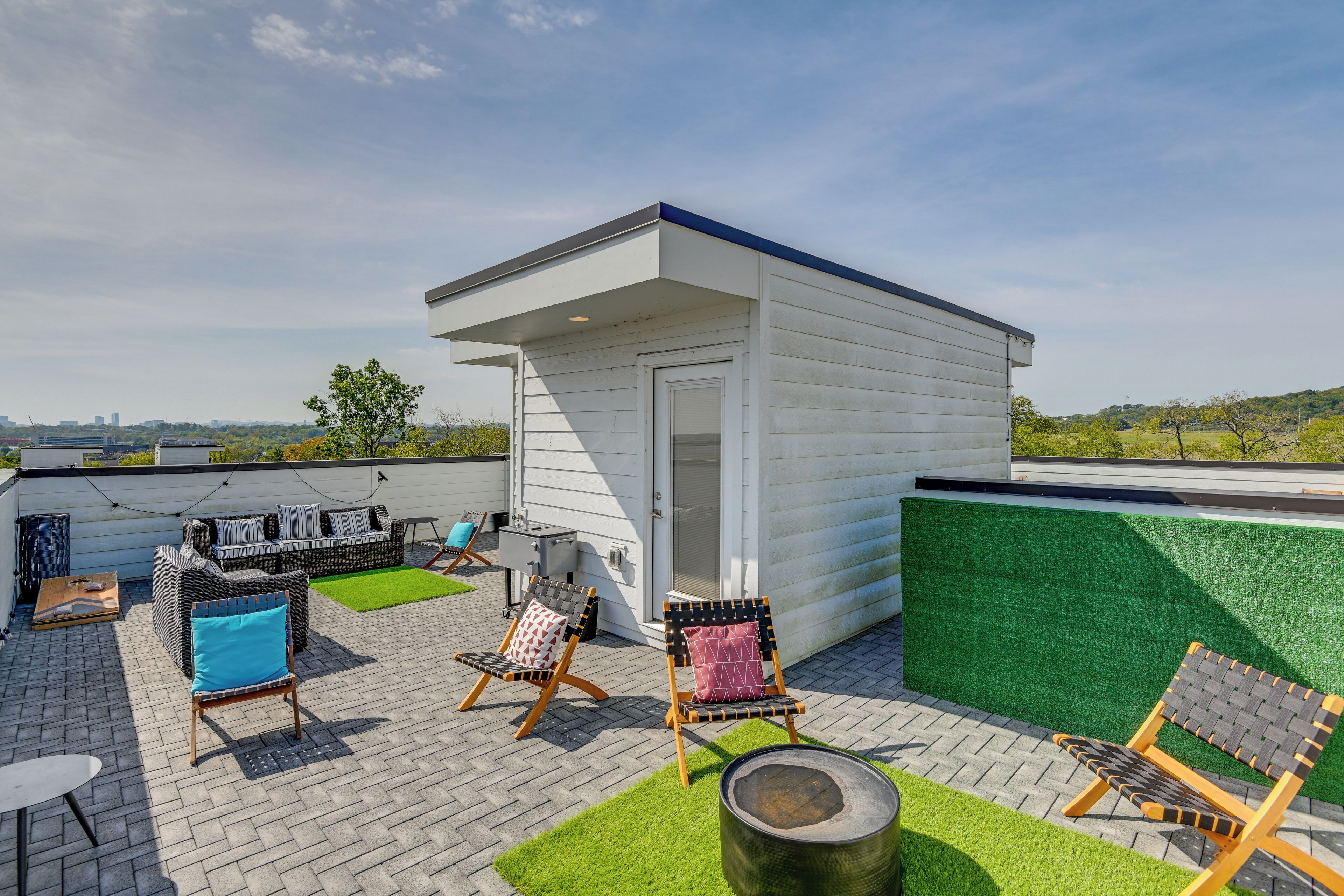 A rooftop patio with outdoor seating, a small building, and a view of the city skyline.