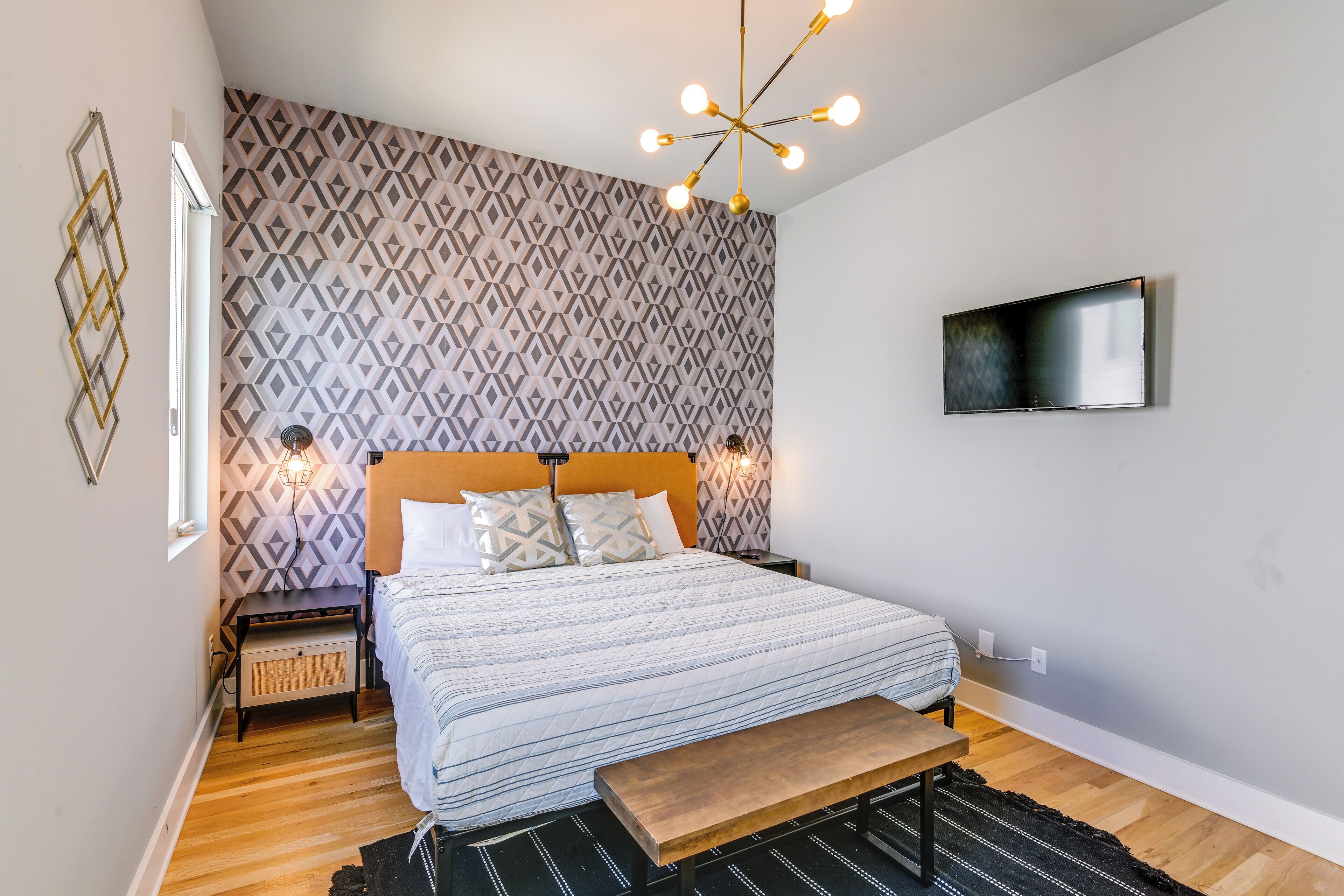Una camera da letto moderna con un letto, comodini, una panca, una TV e carta da parati decorata.