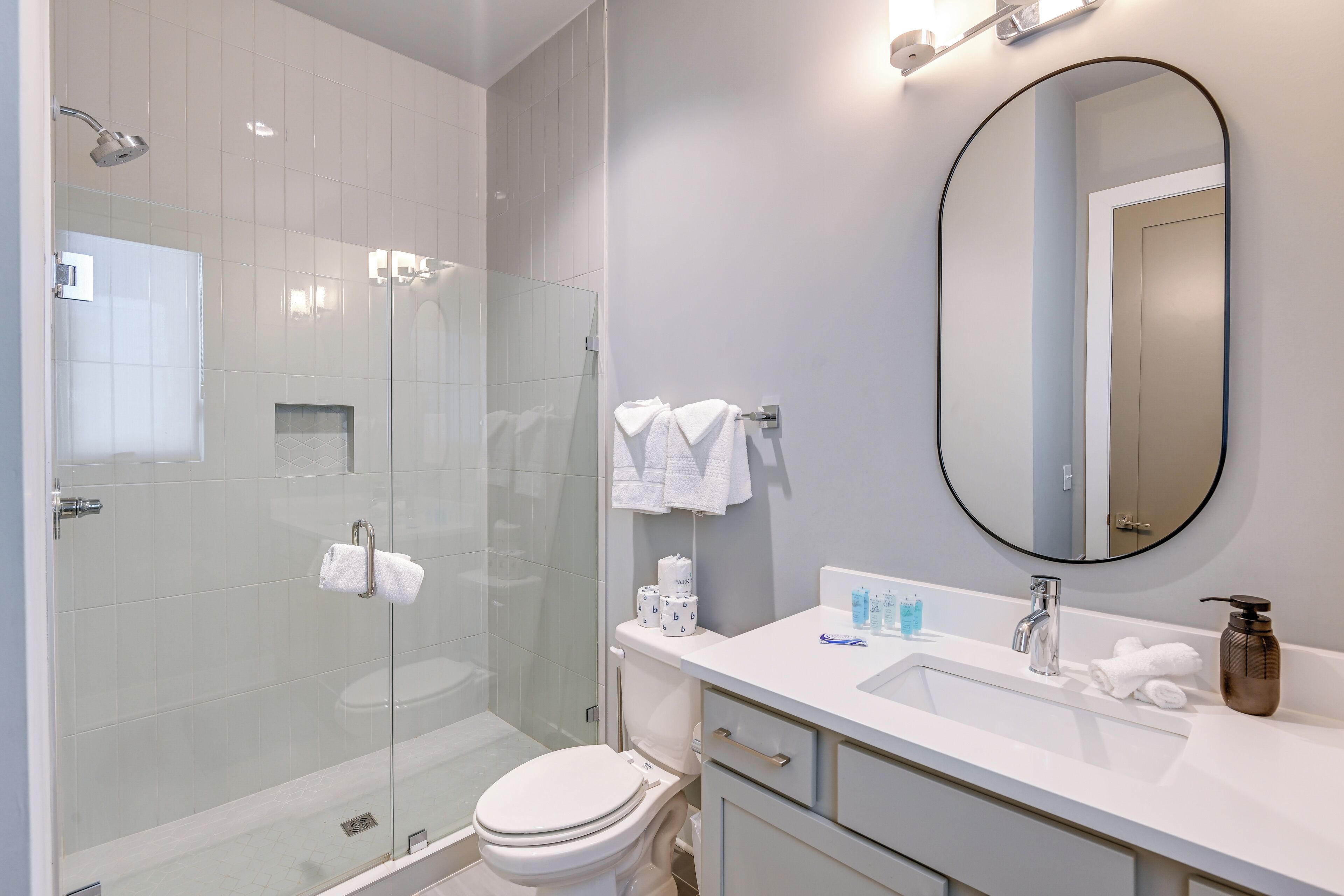 Une salle de bain moderne avec une douche à parois de verre, des toilettes, un lavabo équipé de produits de toilette et un miroir.