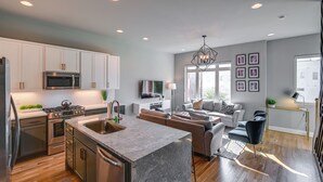 A modern kitchen with stainless steel appliances, a marble island, and a dining area with a sofa and chairs. - Nashville Townhome w/ Rooftop Balcony & Game Room! (Nashville)