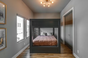 Een slaapkamer met een stapelbed, grote ramen, een plafondlamp en een kledingkast.