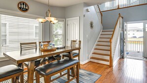 A dining area with a wooden table, chairs, and a chandelier. There is a staircase leading to an upper level. - Inviting Norfolk Family Retreat: 1 Block to Beach! (Norfolk)