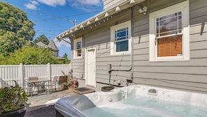 Un jacuzzi situé devant une maison dotée d’une terrasse, d’une clôture en bois et d’une petite table avec des chaises.